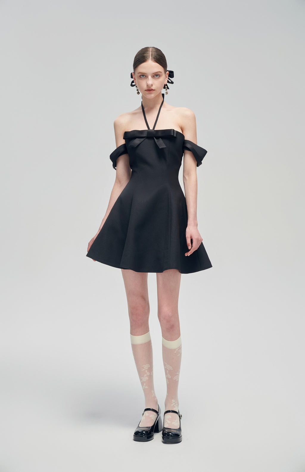 Nero Ritratto Off-Shoulder Dress in black with A-line silhouette, double off-shoulder straps, and halter neckline, styled with sheer socks and black heels.