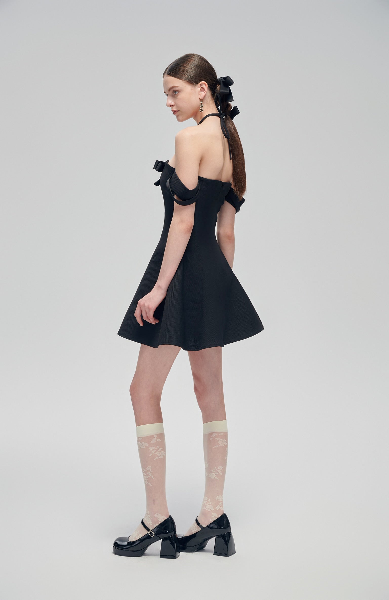 Nero Ritratto Off-Shoulder Dress in black with double off-shoulder straps and A-line silhouette, styled with sheer floral socks and black heels.