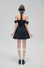 Back view of Nero Ritratto Off-Shoulder Dress featuring double off-shoulder straps and A-line silhouette in black. Styled with bow heels and sheer socks.